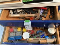 Drawer with wooden-handled claw hammer, hand tools, and small packaged fasteners such as wall anchors and screws.
