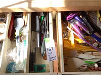 Top view of three drawers containing the assorted kitchen utensils and flatware, showing knife handles, peelers, spatulas and other tools.
