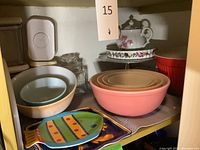 Full view of nested pink/peach Pyrex bowls with additional bowls, serving dishes, and cake stand arranged on shelf.