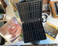 Top view of the open waffle maker showing four square waffle sections and one waffle recipe book titled 'Waffles From Morning to Midnight'.