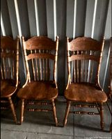 Four vintage solid wood chairs in a row, showing front view with carved floral backrests and turned spindles.