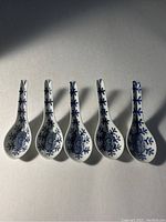Top view showing all five ceramic soup spoons with blue floral designs on white background.