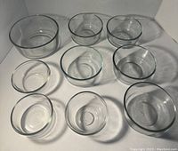 Overhead view showing all nine clear glass mixing bowls in various sizes arranged on a white surface.