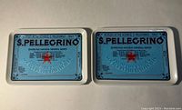 Two vintage metal trays side by side with S. Pellegrino label and branding