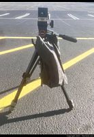 Tripod set up with three legs fully extended on asphalt surface, showing general shape and use condition.