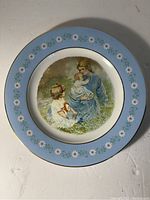 Full view of vintage Avon commemorative plate featuring the 'Tenderness' illustration showing a woman and two children sitting in grass with blue floral border.