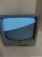 Front view of the Exxis ES-12 video monitor powered on showing a blue screen with scan lines and front panel controls.