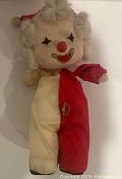 Full body view of the vintage Faratak clown showing its cream and red colored costume, wind-up key, and yarn hair curls.