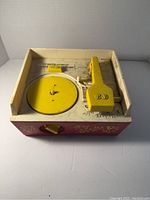 Front view of vintage Fisher Price music box record player; yellow turntable and tonearm on red cream body with decorative accents.