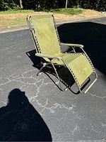 Side view of vintage green lake lounge chair showing reclining metal frame and green fabric stretched and laced around frame. Fabric discolored and worn.