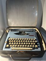 Open typewriter in black carrying case showing the baby blue typewriter with cream keys and black background inside the lid.