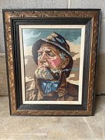 Front view of the framed needlepoint portrait of an old man with a pipe, showing artistic needlework and decorative frame.