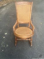 Front view of the vintage wooden rocking chair showing cane seat and backrest.
