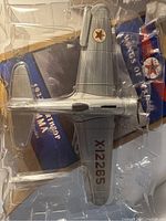 Top-down view of silver Northrop Gamma model airplane in clear plastic tray with blue box and 'Wings of Texaco 1932 Northrop Gamma' text visible beneath.