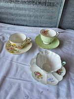 Overview of the three teacup and saucer sets displayed on a sheet, showing different floral designs and styles.