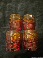 Four skull-shaped drinking glasses with amber and red coloring displayed on black background.