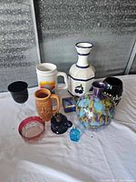 Overview of assorted ceramic and glass items including vases, steins, mugs, bottles, and ashtray
