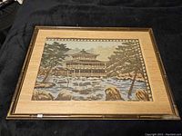 Full view of the framed tapestry showing an Asian style building scene with trees and rocks