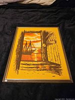 Wide angled photo showing framed tapestry artwork with ship at sunset through open door.