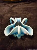 Blue glass dish shown from above on dark fabric surface, highlighting its tri-fold shape and glossy finish.