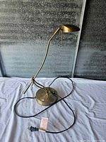 Full view of brass adjustable desk lamp placed on white cloth against corrugated metal background.