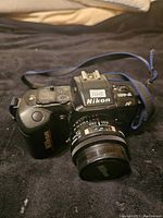 Photo showing Nikon F-401 camera front with attached Nikon AF lens and blue strap, displaying camera body and lens details.