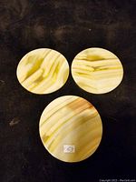 Photo of three round ceramic or marble trivets in varying sizes showing their natural stone pattern in beige and brown tones on a black background.