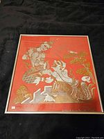 Framed Asian themed artwork with traditional figures and motifs on orange background