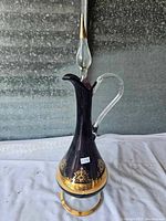 Full view of the vintage glass decanter showing deep purple body, clear glass handle, gold decorative band at the base, and tall stopper with gold tip.
