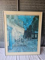 Framed art print showing Vincent Van Gogh's Night Cafe in blue tones with tables and buildings under a starry sky.