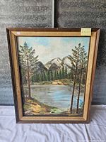 Full view of framed landscape painting showing mountain lake, trees, and background mountains.