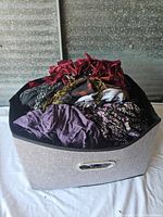 Storage bin filled with assorted folded women's clothing including scarves and tops in various colors and patterns.