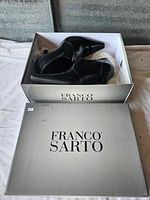Pair of black heels inside a silver Franco Sarto shoebox.