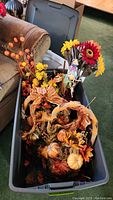 A plastic bin filled with assorted autumn-themed faux floral decorations, including sunflowers, pumpkins, and leaves.