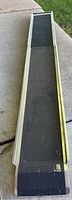 Full view of aluminum ramp extended on concrete surface showing non-slip black grip tape and raised edges.