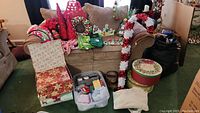 Overall lot view showing couch covered with Christmas stockings, tinsel candy canes, decorative boxes, small figures, and a basket of items with towels and ribbons.