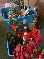 Photo showing plastic tote bins filled with artificial Christmas trees, red poinsettia floral arrangements, and a nutcracker figurine.