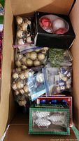 Overhead photo of a box filled with multiple bags and boxes containing assorted Christmas ornaments in gold, white, and novelty snowman styles.