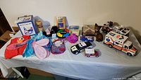 Photo showing a variety of games and toys including toy emergency vehicles, board games Simon, Mad Gab, Bingo, pink fairy wings, Elmo plush, and kids' purses arranged on a table.