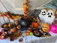 Overall view of Halloween and fall themed decorations including pumpkins, ghosts, garlands, bucket, and small decor pieces on a white tablecloth.