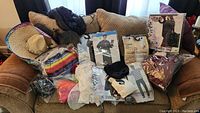 Multiple Halloween costumes and accessories arranged on a couch including sombrero, masks, and inflatable packaging