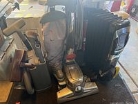 Overview of Kirby vacuum with fabric bag, upright metal body, multiple cleaning accessories, and black ceramic heater next to it.