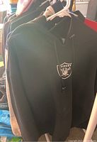 Black Raiders hoodie on rack with other coats and jackets visible behind it.