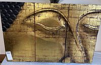 Front view of large modern art panel depicting Asian-inspired face in textured gold and bronze.