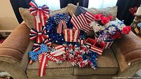 View of various patriotic home decor items arranged on a couch including ribbons, flags, floral arrangements, wreath, and signs.