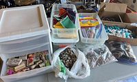 Wide view of multiple plastic containers filled with classroom craft supplies, small rocks in bags, and stamps.