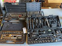 Photo showing multiple tool sets arranged in open cases displaying sockets, ratchets, and various hand tools including pliers and wrenches.