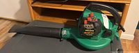 Side profile view of handheld Weed Eater BG 6558 blower vac featuring blower tube attachment, green and black body, placed on table surface.