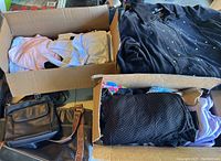Two cardboard boxes containing folded women's clothes and a studded black shirt with several handbags located beside the boxes.