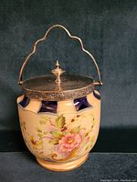 Front view of biscuit jar showing floral design and silver lid with finial